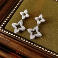 Macro view of silver clover earrings with inlaid zircons on dark green velvet background - Silver