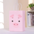 Sacchetto regalo in carta rosa con maialino e manici bianchi su sfondo di una libreria - Motivo a Maiale (Rosa Chiaro)