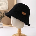 Detail of black fleece bucket hat with brown leather logo tag on a wooden mannequin - Black