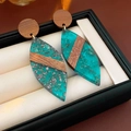 Detalle de pendientes de hoja en resina verde azulado y madera oscura con purpurina - Azul