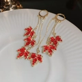 Macro shot of gold earrings with red maple leaf gems and delicate tassel chain detail - Red Maple Leaf Tassel Style