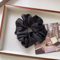 Detail of elegant black satin scrunchie with smooth silk texture and rich pleats on a tray - Large / Black