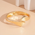 Detail eines goldenen geometrischen Armreifs mit Federscharnier auf minimalistischer Ablage - Gold