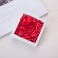 Macro view of red shredded paper raffia filler inside a white square gift box - 20g per Pack / Red
