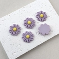 Macro shot of purple resin daisy flower charms with yellow center on white stone plate - Light Purple