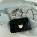 Black quilted chain crossbody bag with gold hardware placed on a light green suit jacket - Black