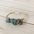 Detail van de koperdraad gewikkelde gouden armband met drie blauwe apatietkristallen - Apatiet