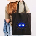 Black canvas tote bag with blue Greek Evil Eye graffiti print on a model shoulder - Design S-Abstract Line Eye-Black