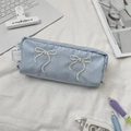 Detailed close-up of light blue pencil case with white ribbon bow embroidery and zipper - Light Blue
