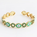 Detailed close-up of gold-plated open bangle with green zircons and evil eye charms - Oval Green