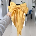 Elegant large yellow satin bow hair clip held by hand in a modern home setting - Turmeric
