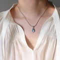 Detailed view of sea blue water-drop pendant on silver snake chain worn by a model - Blue Waterdrop Necklace / Silver