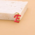 Letter E gold-plated pendant with magenta enamel finish on a textured beige stone base - Enamel Letter-E
