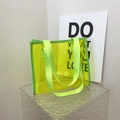 Neon green transparent PVC tote bag with matching nylon handles on a textured block - Green