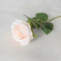 Single stem artificial velvet rose in cream pink with green leaves on white plush rug - Champagne
