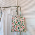 Close-up of floral cotton canvas tote bag with red rose prints hanging on a rack - Green Base Red Rose