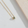 Dettaglio collana dorata con ciondolo cilindrico in zircone blu su pelle bianca - Blu Lago