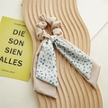 Detalle de coletero de satén beige con cinta floral sobre una tabla de madera decorativa - Azul Bruma Doble Capa