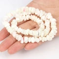DIY irregular white shell bead bracelet with red spots on a palm, neutral background - Irregular White