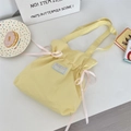 Close-up of light yellow canvas tote bag with pink ribbon bows and drawstring details - Yellow
