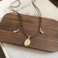 Macro detail of golden oval pendant with spiral texture on brown cord necklace - Gold Pendant + Coffee Rope