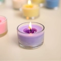 Scented tealight candle in purple glass jar with bright burning flame and blurred background - Purple (Freesia)