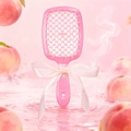 Pink hollow scented hairbrush with a decorative ribbon bow over a peach water background - Peach Scent (Pink)