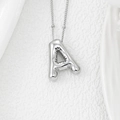 Macro shot of 3D puffy silver letter A pendant on delicate chain over white satin fabric - Letter A Pendant