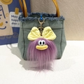 Dettaglio del portachiavi mostro viola di peluche con fiocco giallo su borsa di jeans - Viola