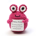 Détail macro d'une poupée grenouille rose au crochet tenant une carte blanche - Grenouille rose rouge