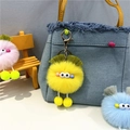 Close-up of yellow plush monster keychain on blue denim bag with metal lobster clasp - Yellow