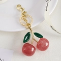 Detailed close-up of glittery red cherry keychain with green leaves and gold metal clasp - Gold + Double Green Leaves Pink Cherry