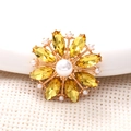 Dettaglio del ciondolo girasole dorato con gemme gialle e finiture di perle bianche - Oro