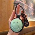 Groene leren ronde sleutelhanger met smiley en zwart metalen haakje op houten achtergrond - Leer-Groen Glimlach