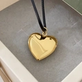 Vista dettagliata di un medaglione a cuore apribile dorato su un cordoncino nero - Ciondolo in acciaio inossidabile + corda nera / Oro 18K