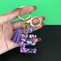 Detail of resin letter E keychain with purple tassel and colorful stones in gold metal - Letter E