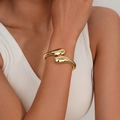 Bracciale rigido dorato a goccia con finitura lucida mostrato sul polso di una modella - Oro