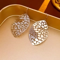 Detailed close-up of silver hollow leaf earrings on a decorative golden tray - Silver