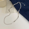 Primer plano de collar de cadena de serpiente plateada sobre denim y página de libro - Plateado
