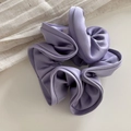 Close-up of a glossy lavender satin scrunchie showing delicate ruffles and texture - Purple