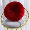 Red circular velvet pumpkin cushion with handcrafted pleats on a stylish metal chair - Red