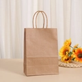 Eco-friendly brown kraft paper gift bag with twisted handles on a warm wooden tabletop - 15x11x6cm Matching Handle / Natural