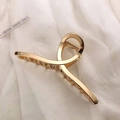 Close-up of large gold metal hair claw clip resting on elegant white silk fabric - KC Gold-Cross