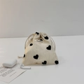 Close-up of cream drawstring storage pouch with black heart patterns and accessories - Champagne Heart