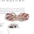 Barrette nœud en or rose ornée de strass roses et transparents sur un magazine - Ruban / Carmin