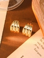 Macro detail showing the ribbed golden metal texture of C-shaped flower earrings on vintage paper - Gold Arched Row