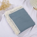 Close-up of a blue cotton waffle baby blanket with decorative cream white fringe tassels - Blue