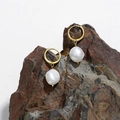 Elegant gold earrings with white irregular baroque pearls hanging on a natural rock - Gold