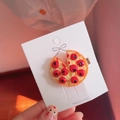 Dettaglio di un fermaglio per capelli a forma di pizza su una carta decorativa - Stile Pizza