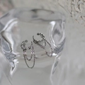 Detail einer silbernen Ohrmanschette mit drei hängenden Ketten auf Glasoberfläche - Silber